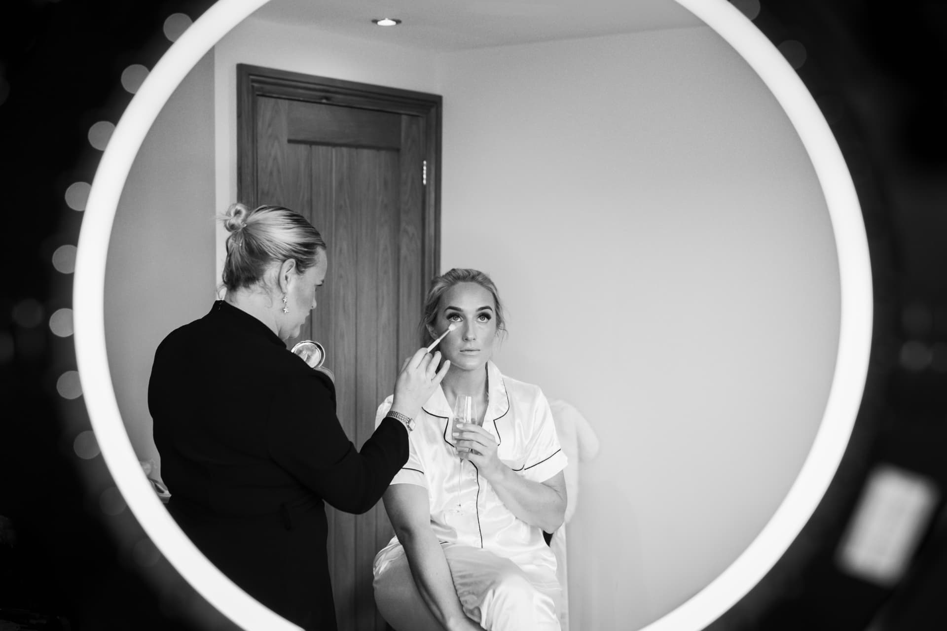 Bride having her make-up done, framed in a round ring-light mirror, black and white